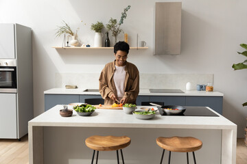 Happy young African American housewife girl slicing fresh vegetables for salad in home kitchen, preparing dinner from organic food ingredients, enjoying cooking hobby, keeping healthy eating
