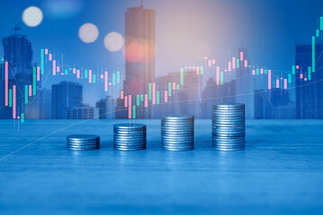Stack of money coin on office desk with blur background of city building and trading graph. Business and financial concept. 
