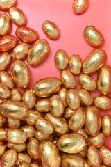 Large and small pile or group of gold, orange and bronze foil wrapped chocolate easter eggs, against a peach orange background.