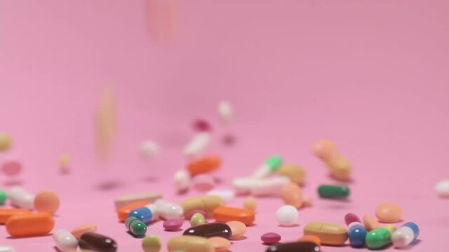 Colored tablets and pills falling down on pink background. Pharmacy medicine and health care concept
