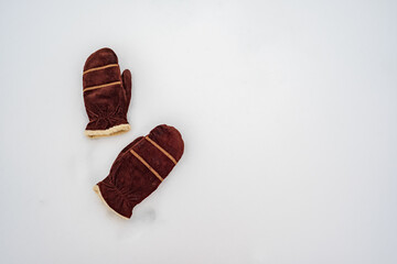 Warm suede brown mittens lie on the pure white snow on a cloudy winter day. Copy space. Top view. 