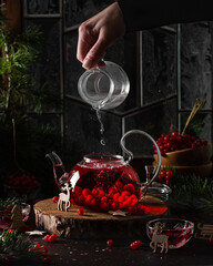Healthy hot drink with red berries viburnum, pouring hot water from glass into teapot . Bubbling tea. Christmas drinks. 