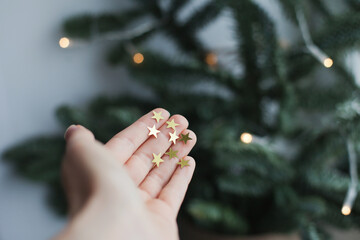 Golden glitter stars on a palm of a hand near christmas tree as festive background