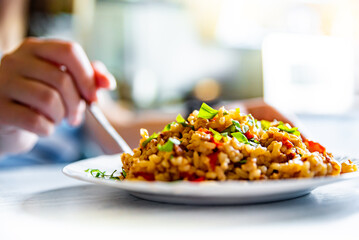 woman hand eating hot rice with meat and vegetables in a white plate