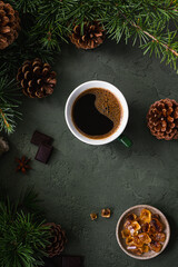 Black coffee in a green cup, chocolate and caramel sugar on a green background with fir branches and cones. Top view
