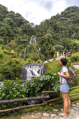 Vertical view of traveler woman with backpack sightseeing waterfall in Colombia jungle. Panoramic view of natural thermal springs in Santa Rosa Cabal valley. Colombia travel destination concept.