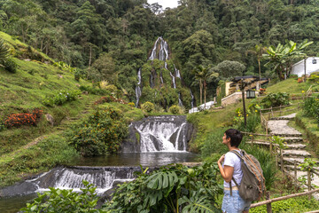 Fototapeta na wymiar Horizontal view of latin american woman sightseeing waterfall in Colombia jungle. Panoramic view of natural thermal springs in Santa Rosa Cabal valley. Colombia travel destination concept.