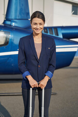 Cheerful lady standing near helicopter on helipad