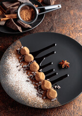 Chocolate truffles on a black plate with chocolate sauce.