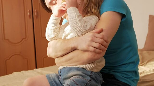 little girl cries, disobeys, screams, hysterical. Dad sits on bed in bedroom, lifestyle real life, home interior, training and upbringing. man tries to comfort and hug, child pushes