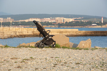 a black baby stroller on the seashore, against the background of the city.