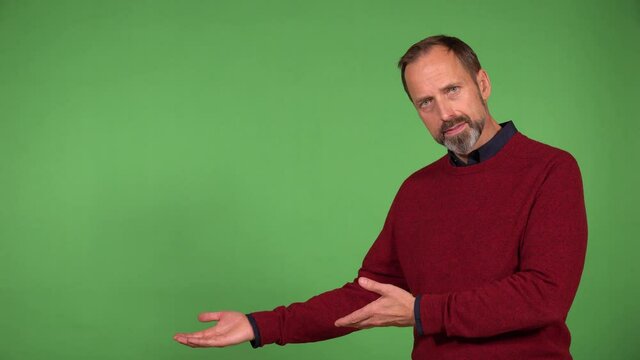 A middle-aged handsome Caucasian man presents something to the camera with a smile - green screen background