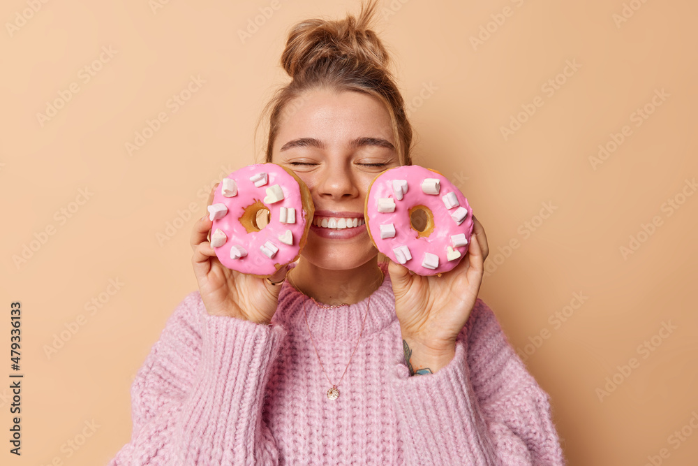 Wall mural tasty food and dieting concept. happy young woman keeps eyes closed smiles broadly holds two doughnu