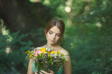 a beautiful girl stands in the forest in greenery with a bouquet of flowers, close-up