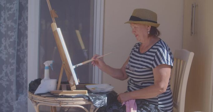 Smiling pensioner lady in striped t-shirt draws painting