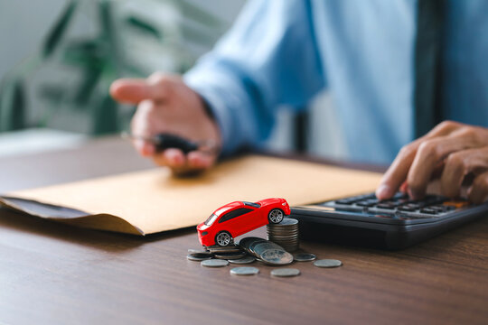  Toy car on stack coins and man holding the key car in hand. after completes the insurance policy or rental documents. Car insurance concept