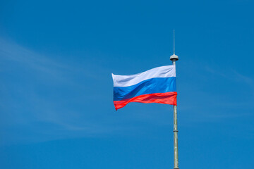 The flag of the Russian Federation flies on a flagpole against a clear and cloudless sky