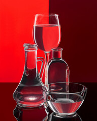 Various glassware with water on a colorful background. The dishes are on a glossy surface.