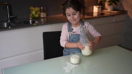 Little girl spills milk when she puts it in a crystal glass to drink it.Concept accidents at home children.