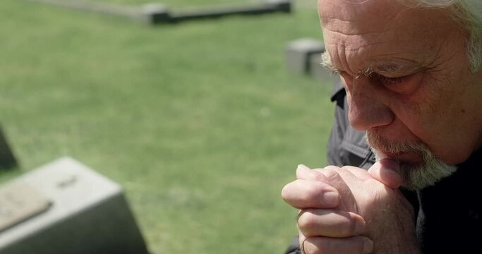 Sad old gray haired man prays on the grave at the cemetery. Sorrow and sadness. Religiuos man, 4k 60p Prores