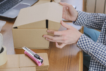 Warehouse employee packs the order of the online store in a cardboard box. The woman closes the...