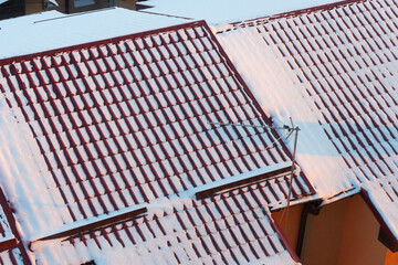 The roof is covered with metal tiles. Snow on the red roof. Snow on the roof of the house. Modern roof covering.