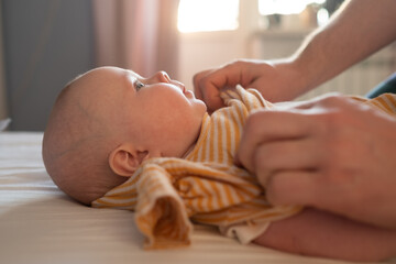 Caucasian parent changing and dressing up baby.