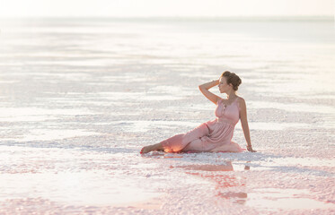 Fototapeta na wymiar a beautiful young girl is sitting in a pink dress on the shore of a salt pink lake