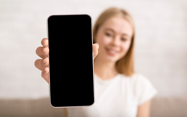 Young woman showing smartphone with big blank screen at camera, lady demonstrating space for mobile...
