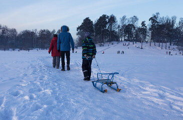 Parents and child with sledges go to ride down the hill