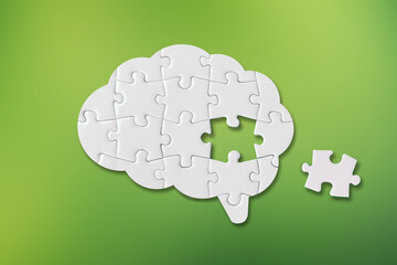 Brain shaped white jigsaw puzzle on green background, a missing piece of the brain puzzle, mental health and problems with memory