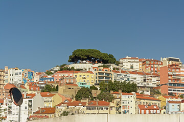 Typical apartment building in pastel colors on a big hill with viewpoint with iconic trees in Lisbon, Portugal