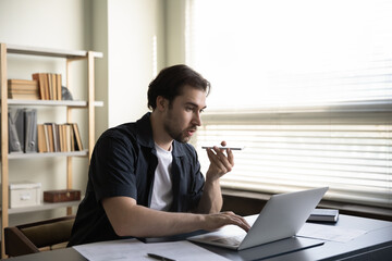 Focused young male employee entrepreneur recording audio message on cellphone or holding...