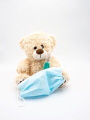 Teddy bear with plastic syringe and medical protective mask - children soft toy on white background