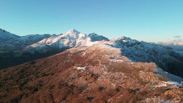 Aerial drone view of a mountain ridge from the Col de Battaglia heading towards the snow capped peak of Monte San Parteo in the Balagne region of Corsica
