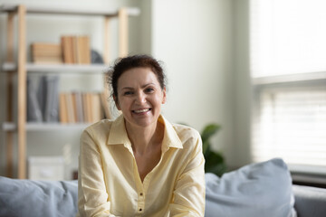 Portrait of happy smiling mature old woman sitting on cozy couch, holding video call distant conversation looking at camera, communicating distantly spending leisure weekend time alone at home.