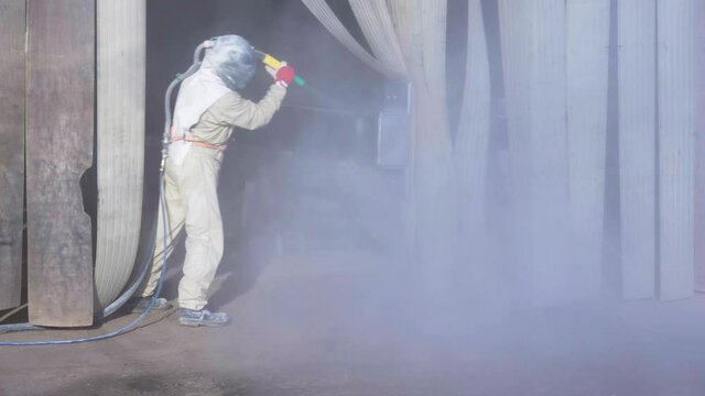 The sandblaster in protective suit and helmet is sandblasting new metal construction. High quality 4k footage