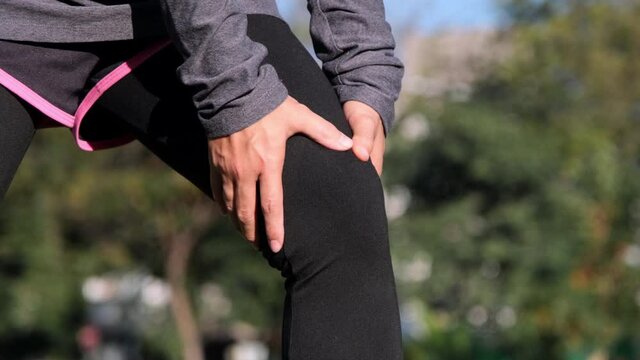 Athlete woman massage leg with thigh muscles pain during running training outdoors. Closeup of female runner touching leg in muscle pain. Muscle sports injury.