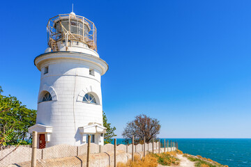 Fototapeta na wymiar Ilyinsky lighthouse at Saint Elijah cape in Feodosiya vicinity, Crimea, Russia. White stone lighthouse in Feodosia at Crimean Eastern coast of Black sea. Popular landmark, travel blog concept
