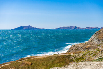 Fototapeta premium Picturesque summer landscape of sea coast with waves on water surface against mountains and sky. Beautiful seascape in sunny day, natural background. Feodosia vicinity, Crimea, Russia