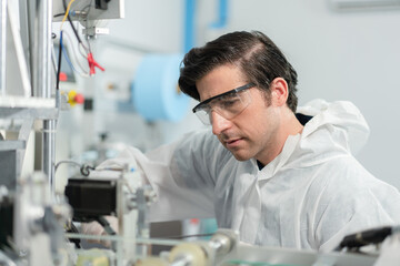 Male Engineers wearing personal protective equipment or PPE to protect and clean checking and inspection machine in the hygienic mask production line at factory industry