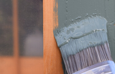 A close up of a decorator's paint brush being used to paint wood a smokey green colour 