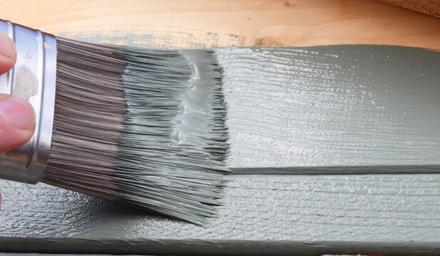 A close up of a decorator's paint brush being used to paint wood a smokey green colour 