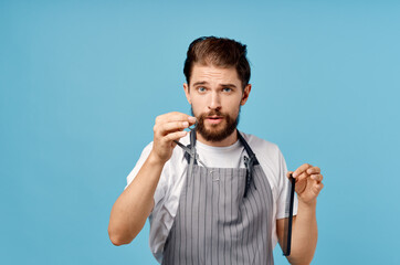 emotional hairdresser in gray apron with scissors and comb on blue background trendy hairstyle