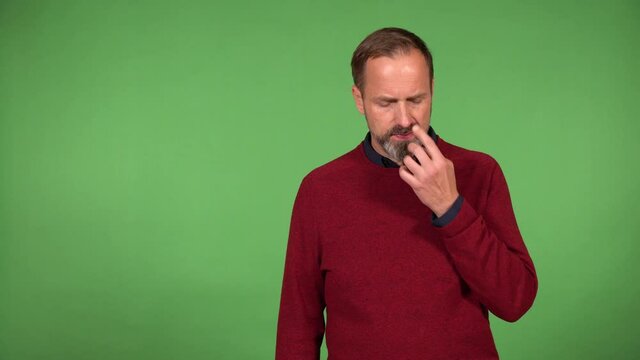 A middle-aged handsome Caucasian man picks his teeth and his nose, then wipes his fingers into his sweater - green screen background