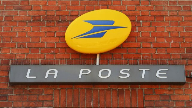 Enseigne et logo de la marque La Poste, c&eacute;l&egrave;bre entreprise fran&ccedil;aise d&rsquo;acheminement du courrier postal, sur le mur en brique rouge d'un bureau de poste &ndash; septembre 2021 (France)