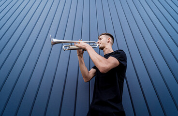 Young street musician playing the trumpet near the big blue wall