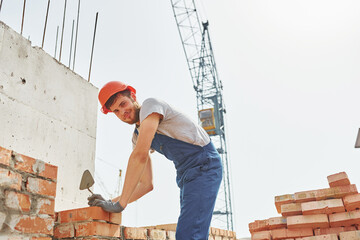 Holding bricks. Young construction worker in uniform is busy at the unfinished building