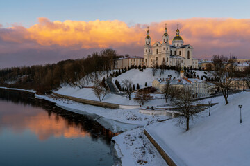 Fototapeta premium Holy Spirits Monastery and Holy Dormition Cathedral on the banks of the Western Dvina River on a winter evening against a pink sunset sky, Vitebsk, Belarus