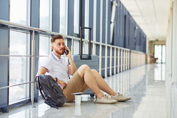 Man sitting on the ground. Young traveler is on the entrance hall in the airport